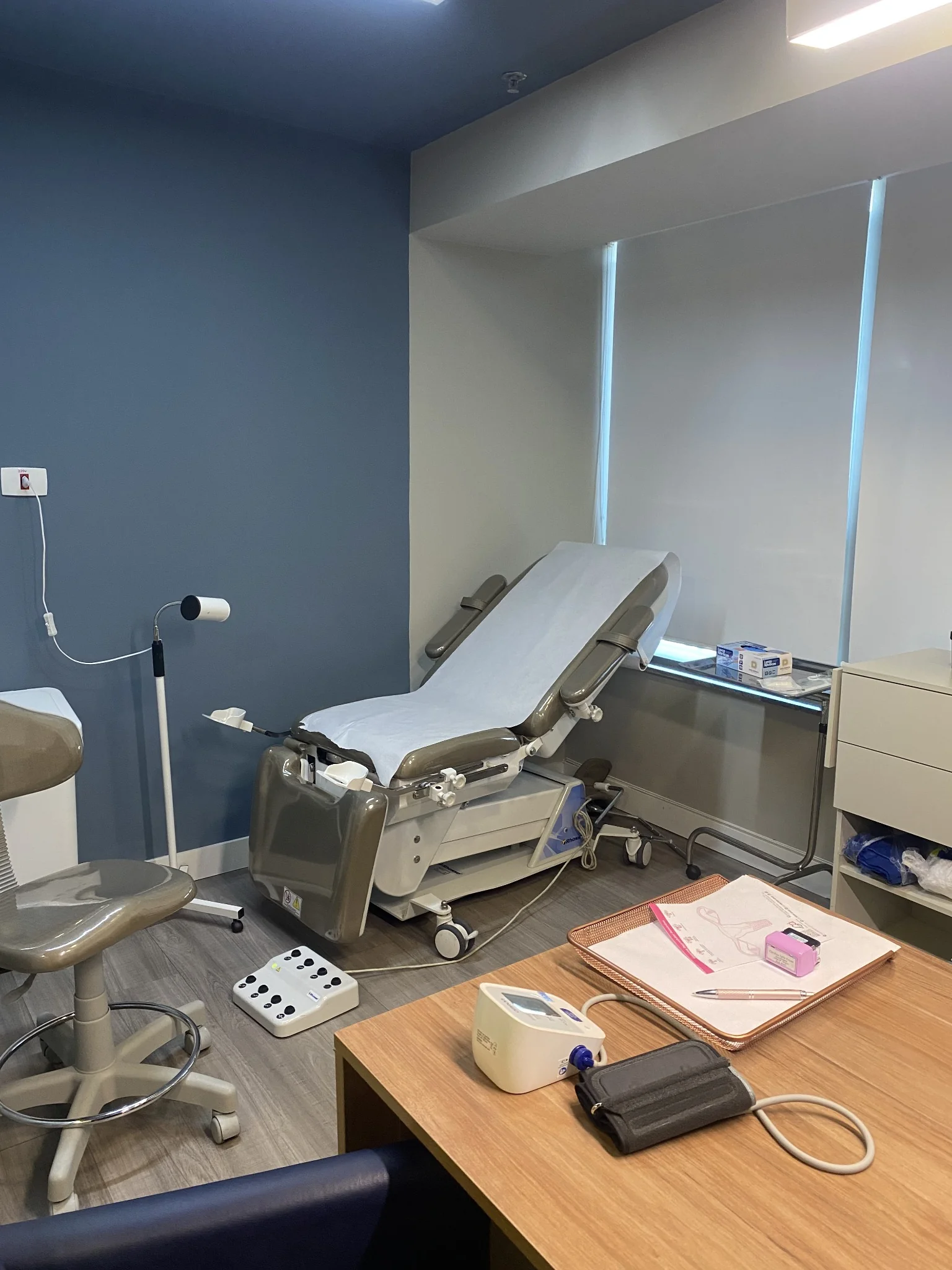 Sala de exame com maca ginecológica, parede azul e banqueta